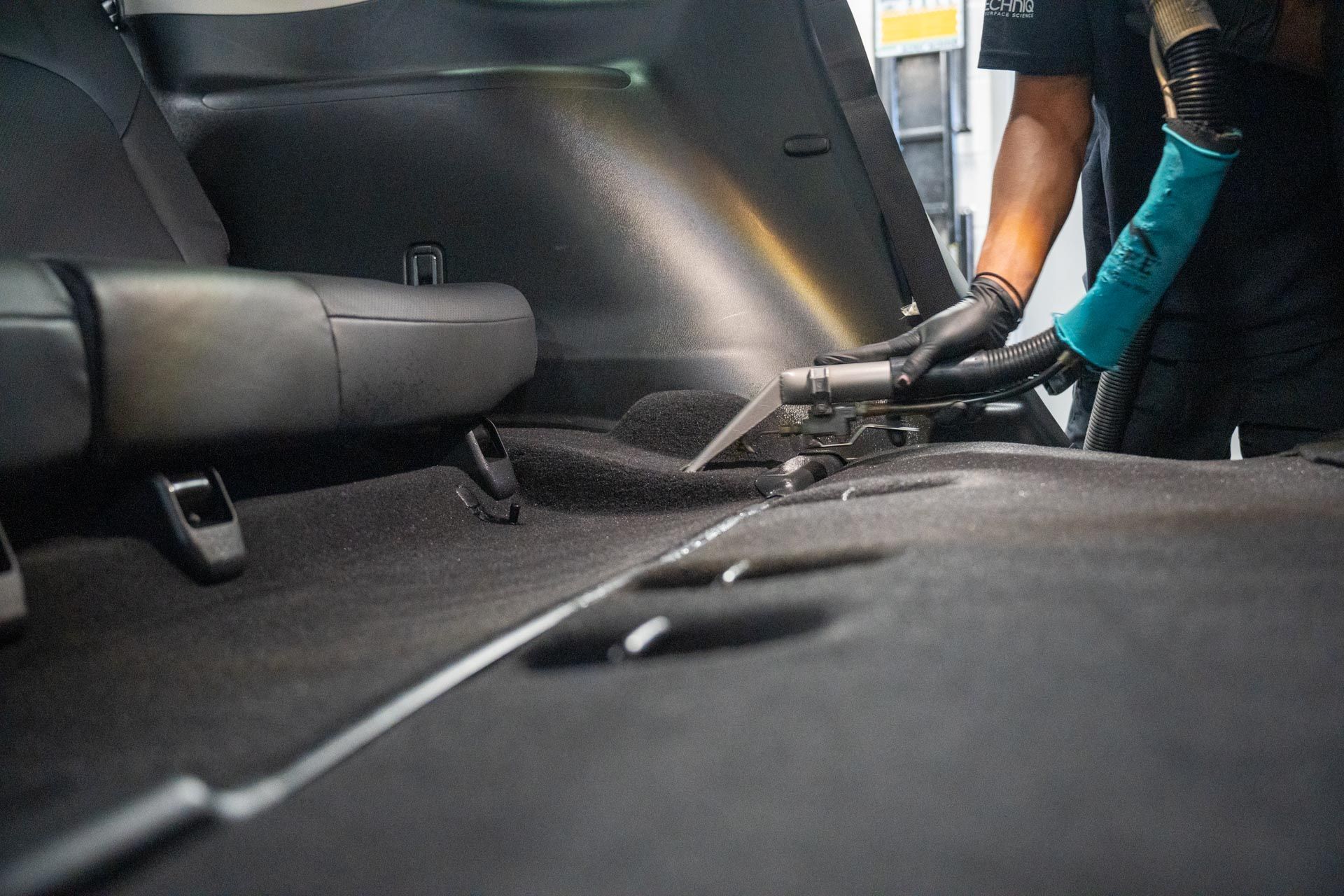 Person vacuuming the back seat of a car interior with a hose attachment