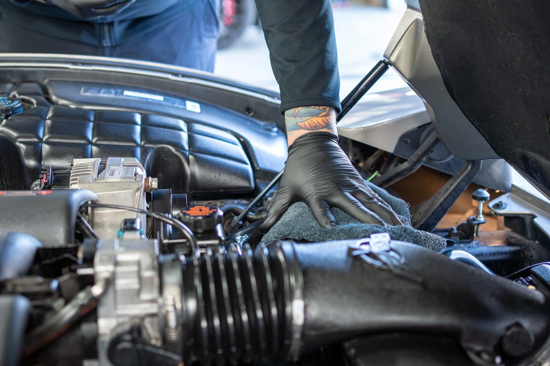 Mechanic in black gloves working under a car hood in an engine bay