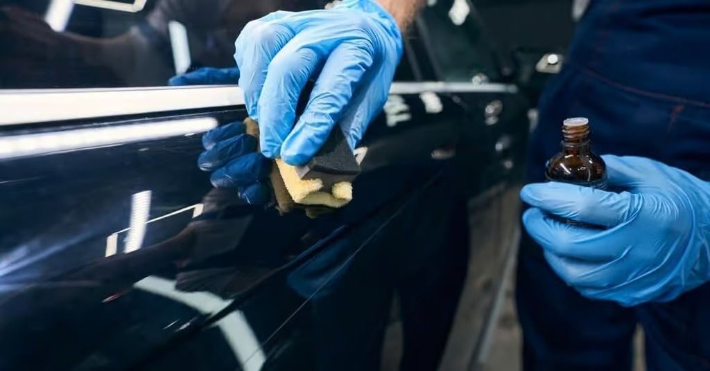 Gloved hands polishing a black car’s glossy surface with a small applicator and bottle nearby