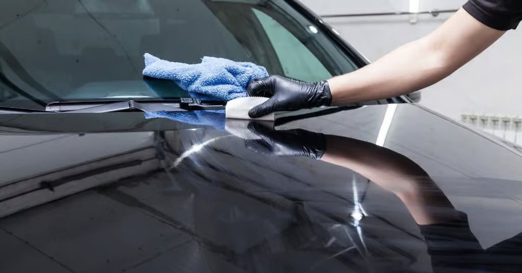 Person polishing a black car hood with a blue microfiber cloth in a garage
