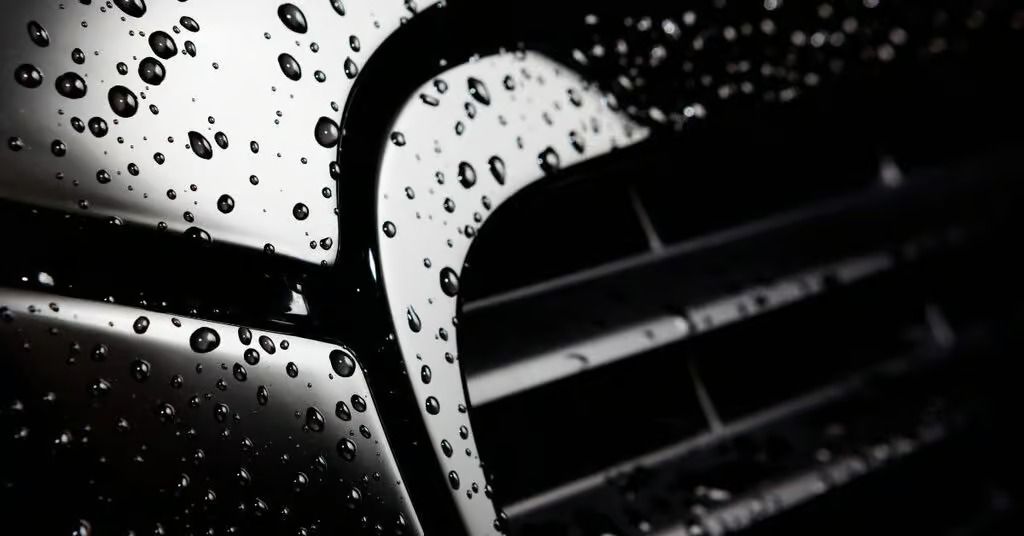 Close-up of a black car grille with raindrops on the hood and chrome trim