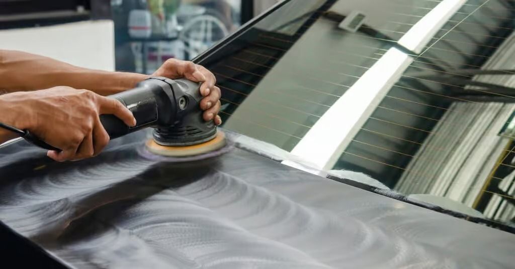 Person polishing a black car hood with a buffer, creating swirl marks in the reflected surface