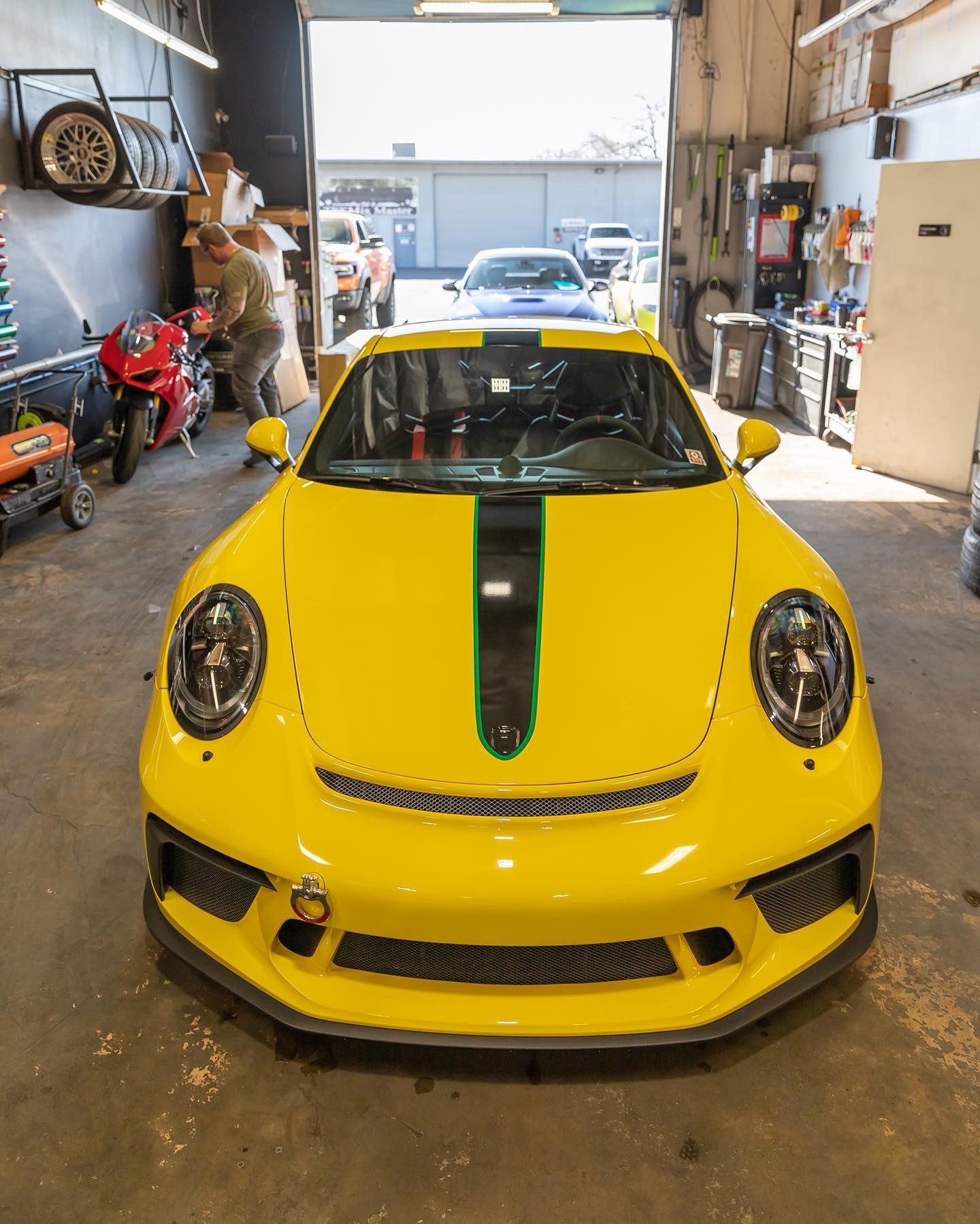 Yellow sports car with a black center stripe parked inside a garage.