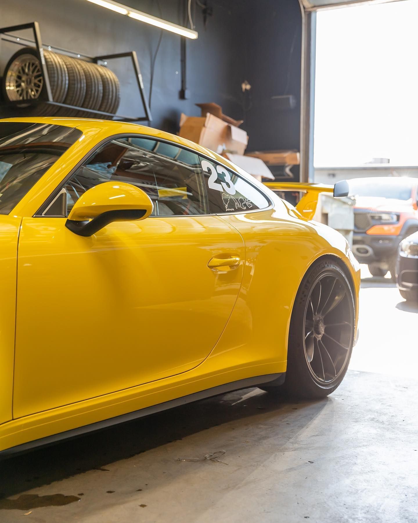 Yellow sports car in a garage, with another car visible near the bright doorway.