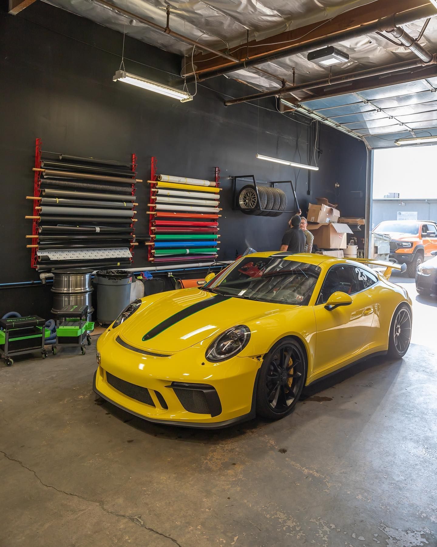 Yellow sports car parked in a garage with stacked colorful rolls on the wall