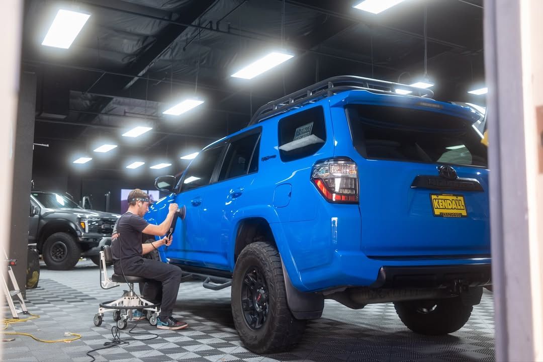 Worker polishing a bright blue SUV inside a car detailing shop