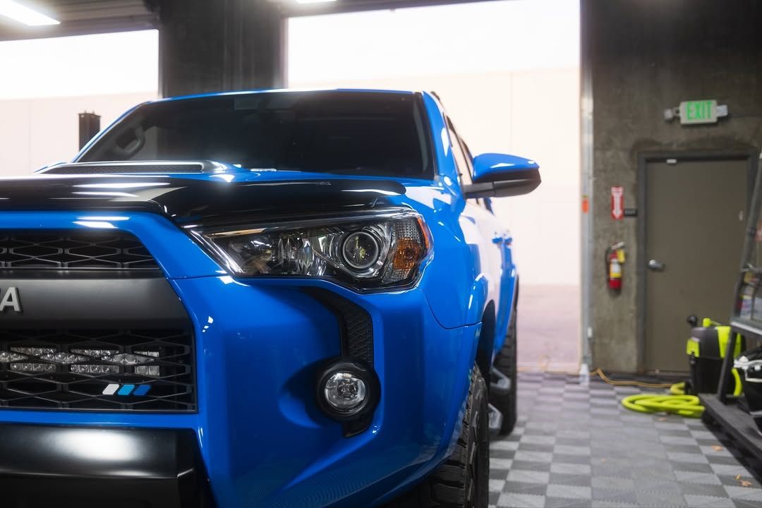 Blue sports car parked inside a garage, front-right view with bright headlights and a black grille.