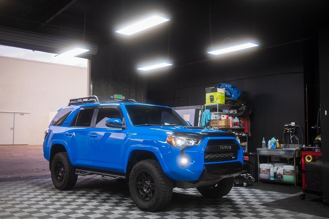 Blue SUV in a garage with bright overhead lights and tools in the background