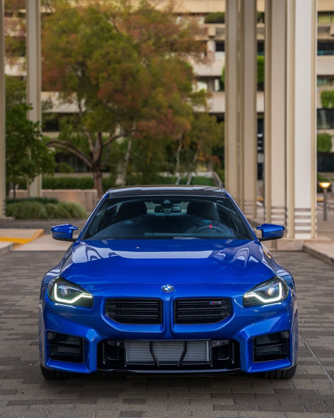 Blue BMW sports car parked outdoors in front of modern columns and apartment buildings
