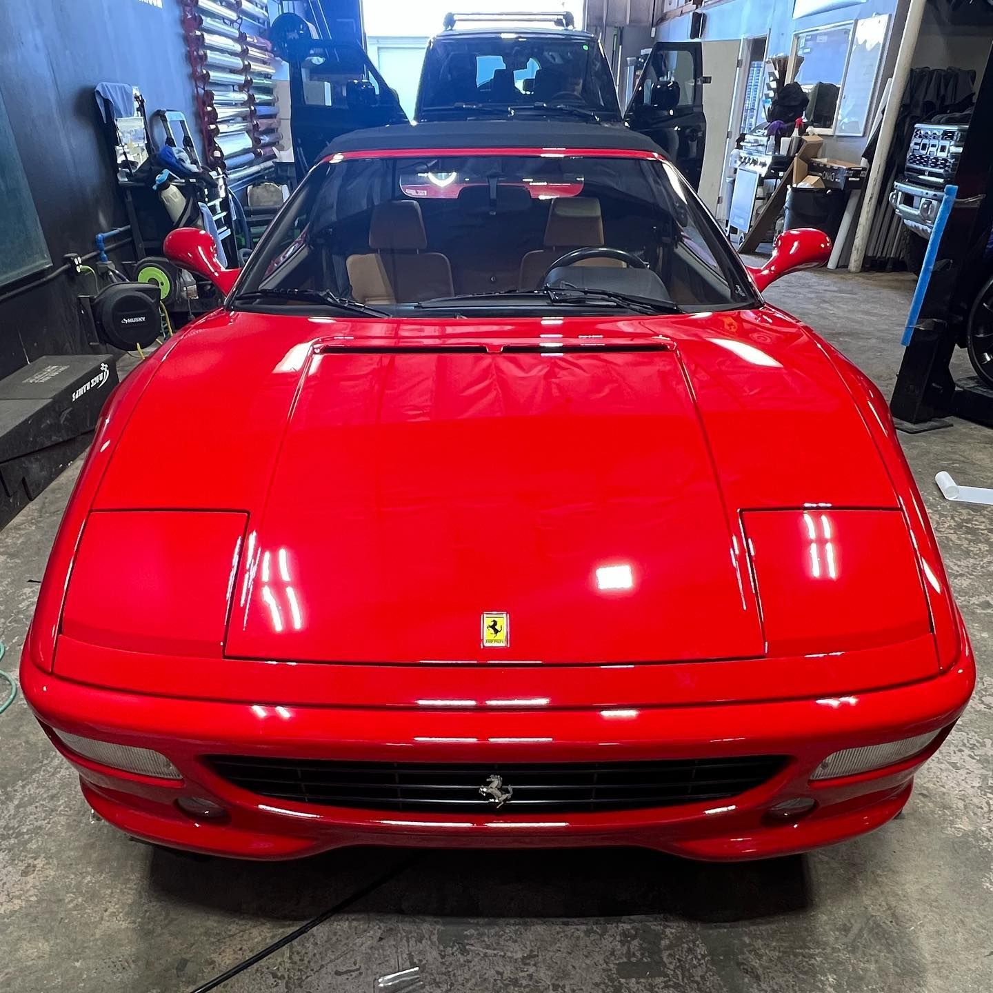 Red Ferrari sports car in a garage, front view with black roof and glossy finish