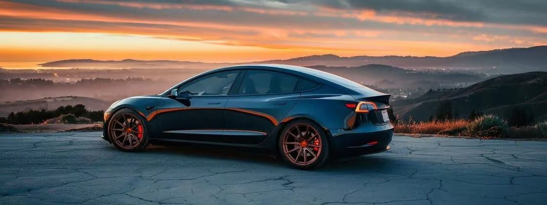 Dark blue sedan with orange accents parked on a hill at sunset, overlooking a misty coastal landscape
