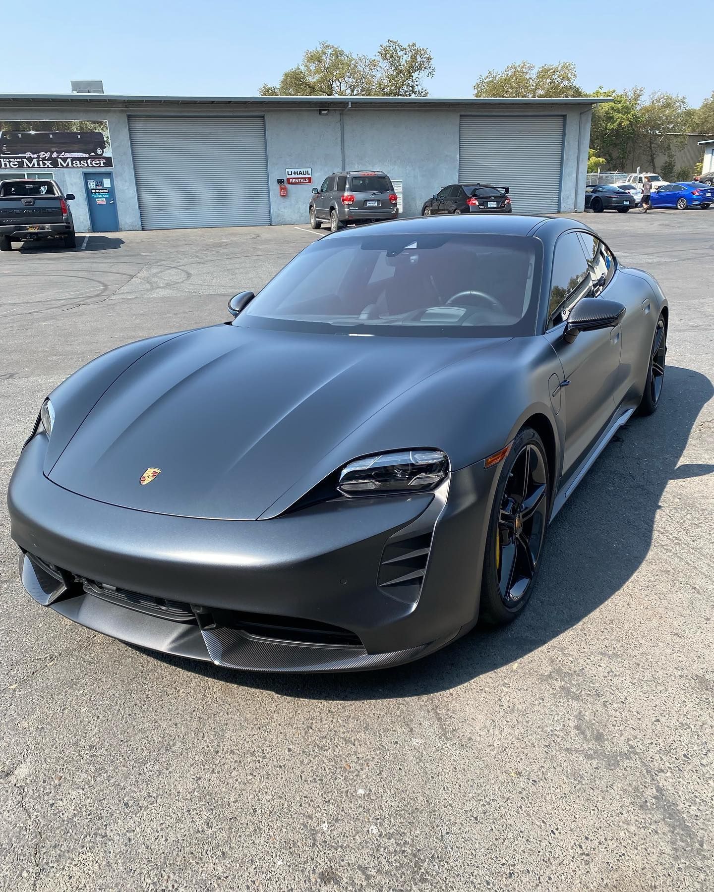 Matte black Porsche sports car parked outdoors in front of a service building.