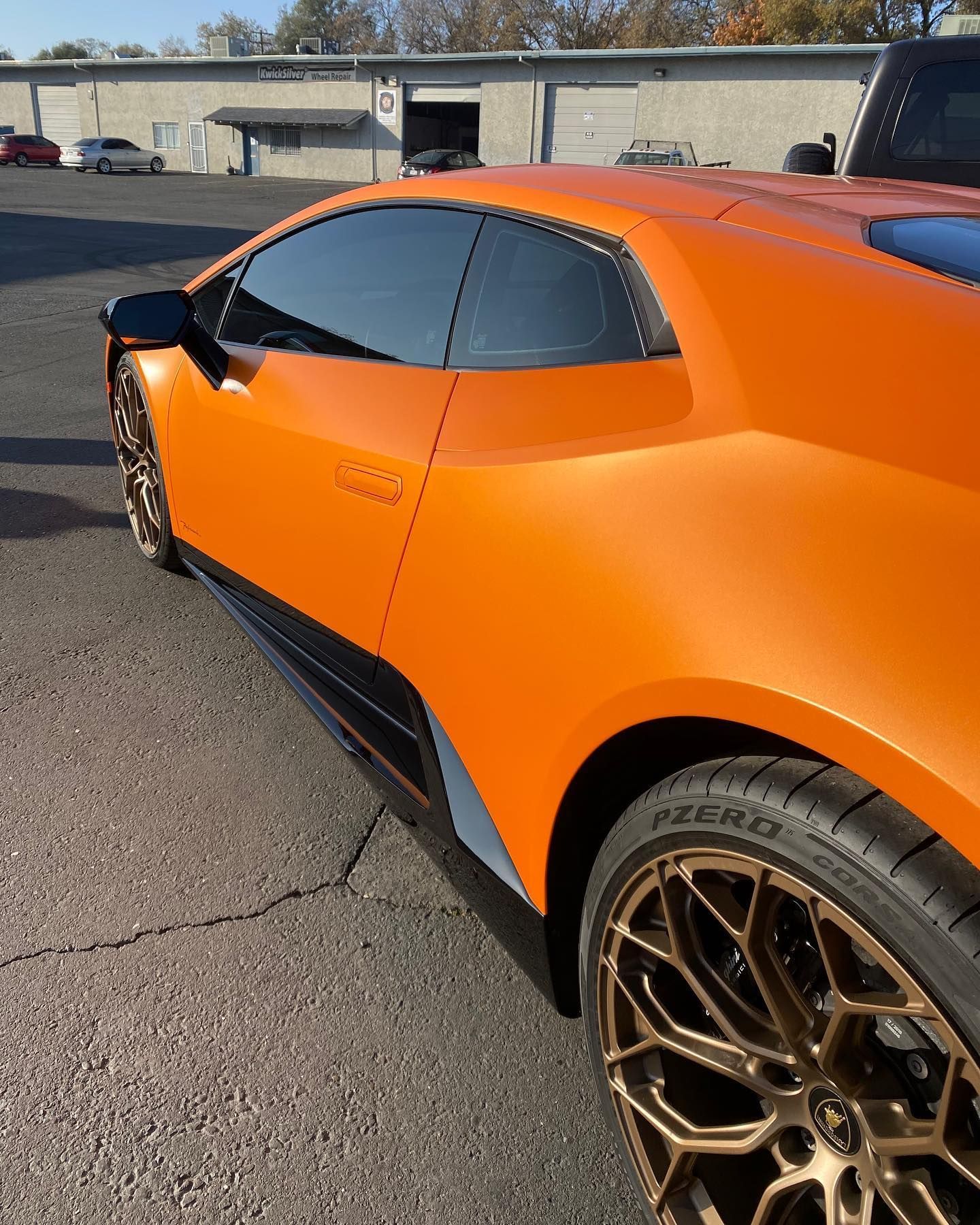 Orange sports car with tinted windows and bronze wheels parked outdoors in a lot.