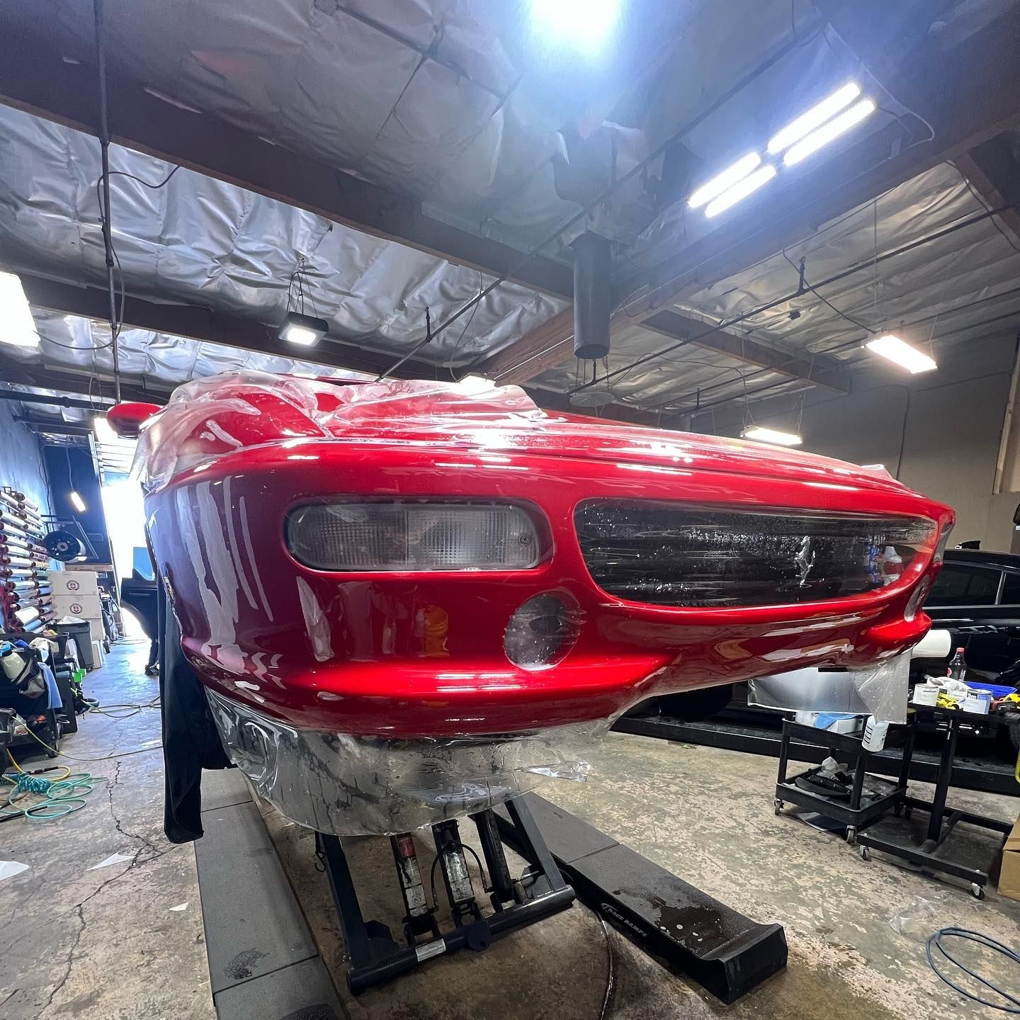 Red sports car front end on a lift in an auto repair shop, with red paint and exposed bumper area
