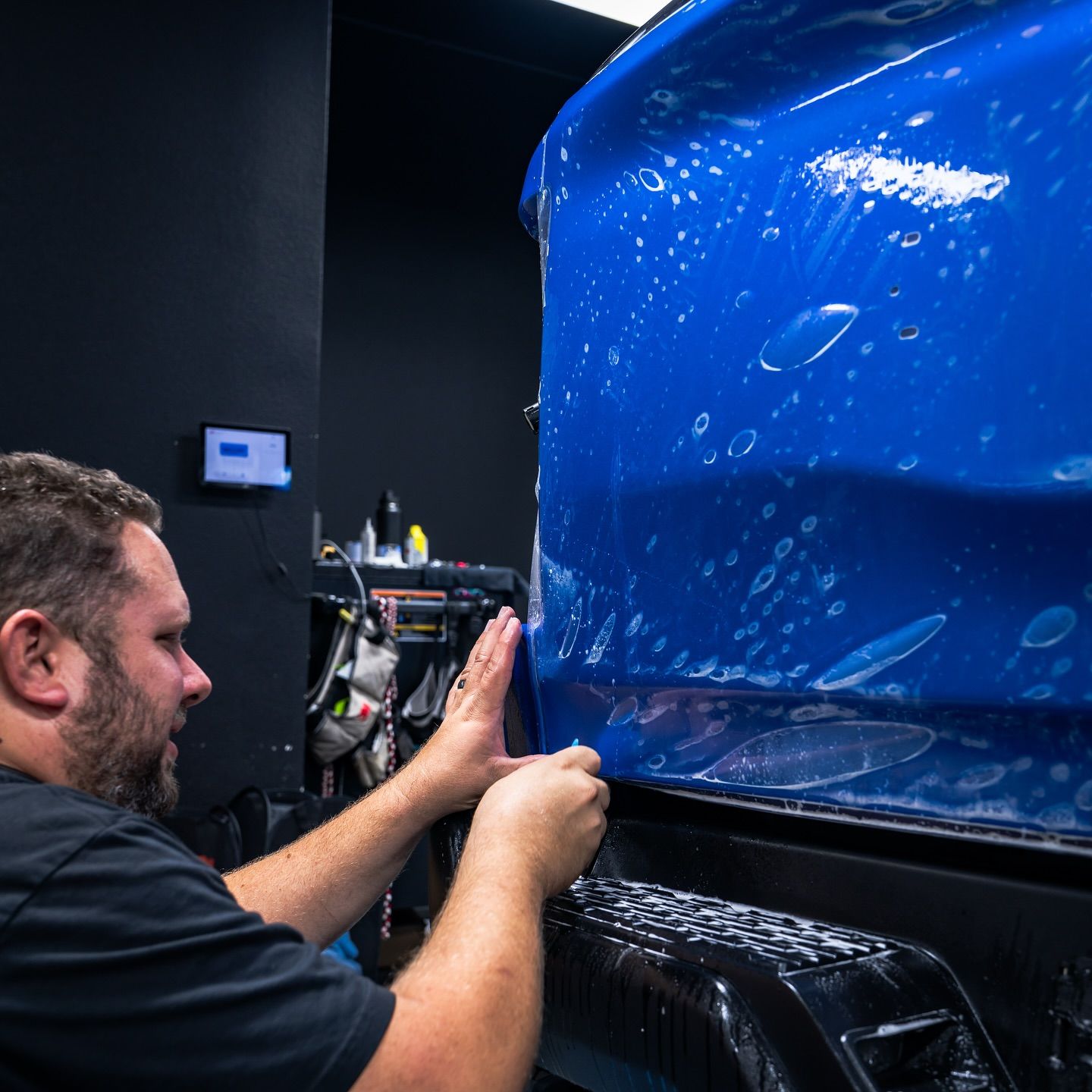 Technician smoothing blue vinyl wrap on a car in a workshop