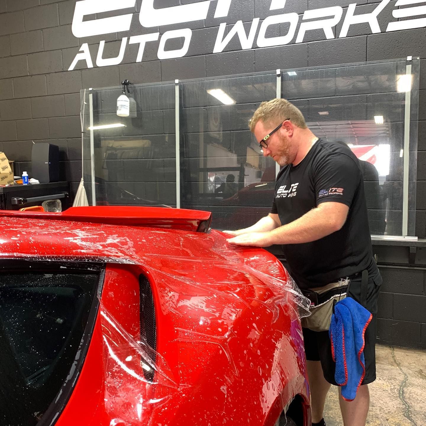 Detailer polishing a red sports car inside an auto work shop
