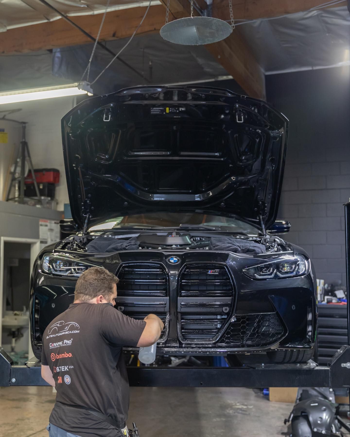 Mechanic working on a black car with its hood open in a garage, front view.