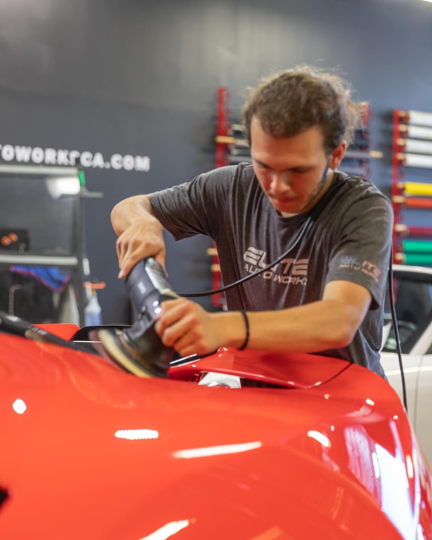 Worker polishing a glossy red car hood in a garage