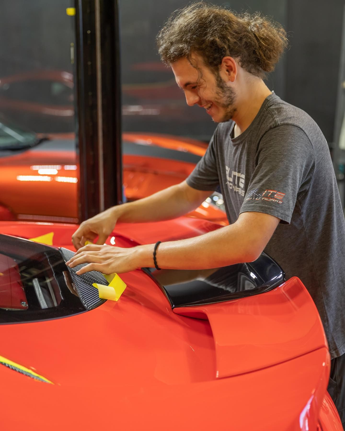 Man polishing a red sports car in a garage, leaning over the hood.