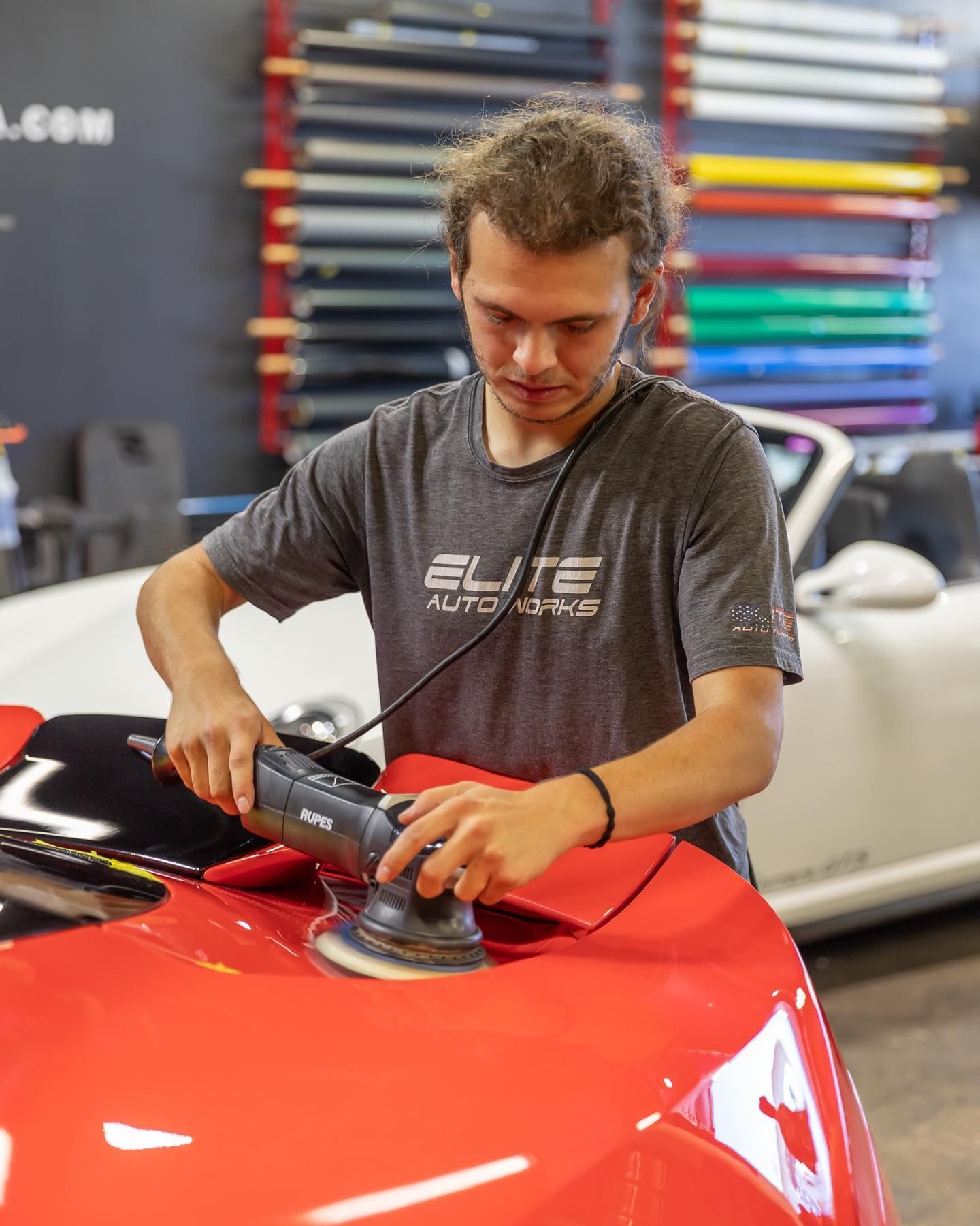 Man polishing a red car hood with a buffer in a workshop