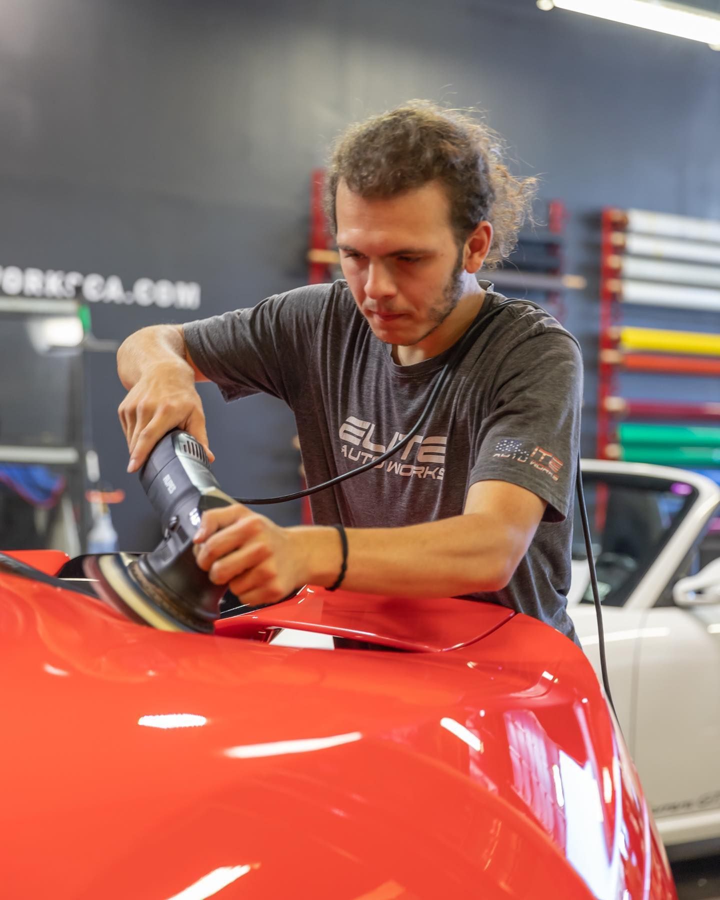 Person polishing a bright red car hood with a buffer in an auto shop