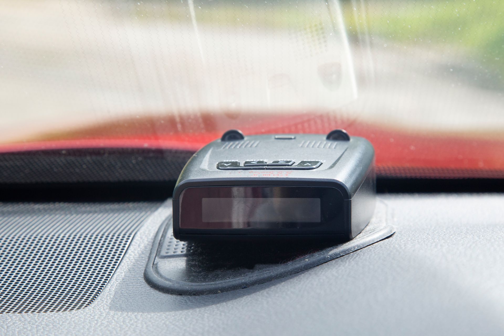 Compact radar detector mounted on a car dashboard, with a blurred road visible ahead.