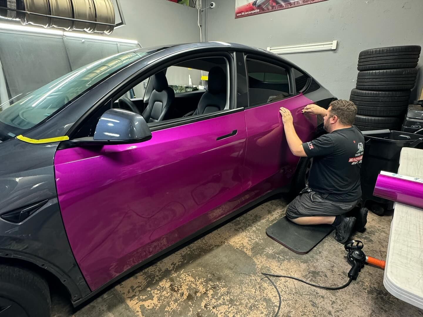 Installer applying purple vinyl wrap to a black SUV in a garage workspace
