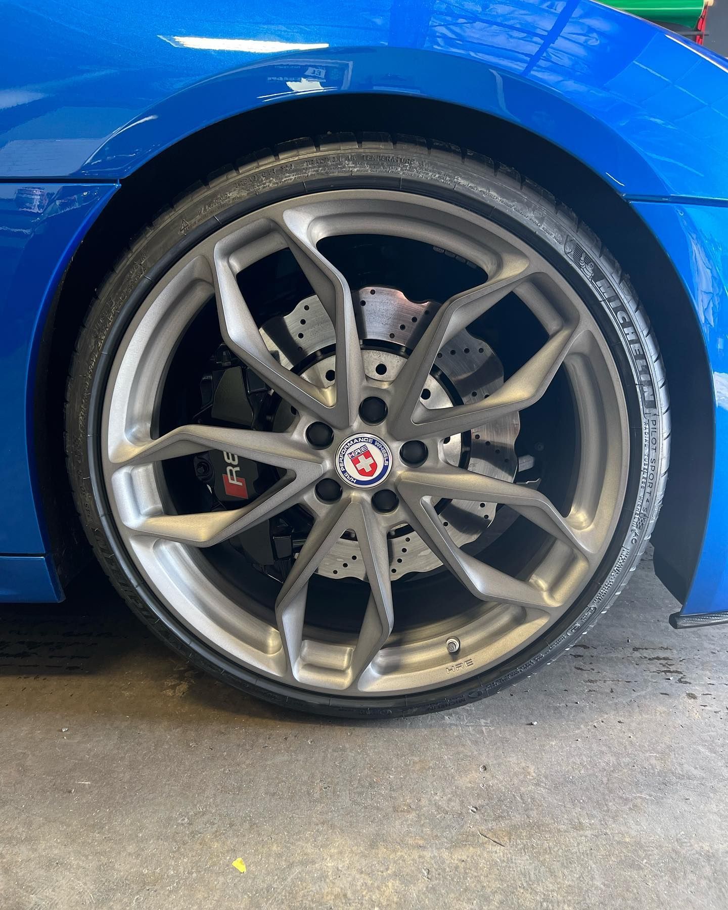 Close-up of a blue car’s front wheel with a silver alloy rim on a wet floor.