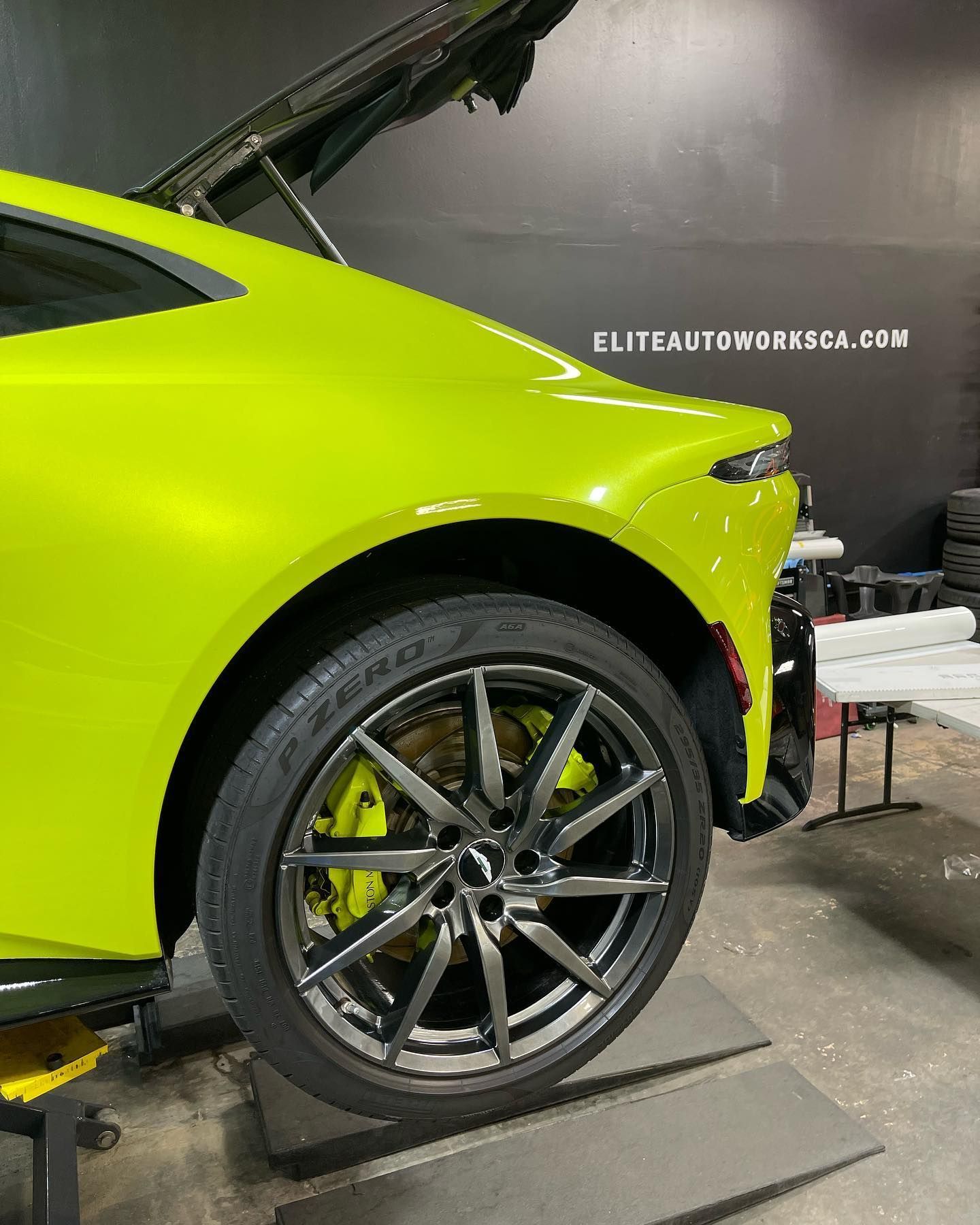 Neon green sports car in a garage, close-up of the front wheel and fender with hood open.