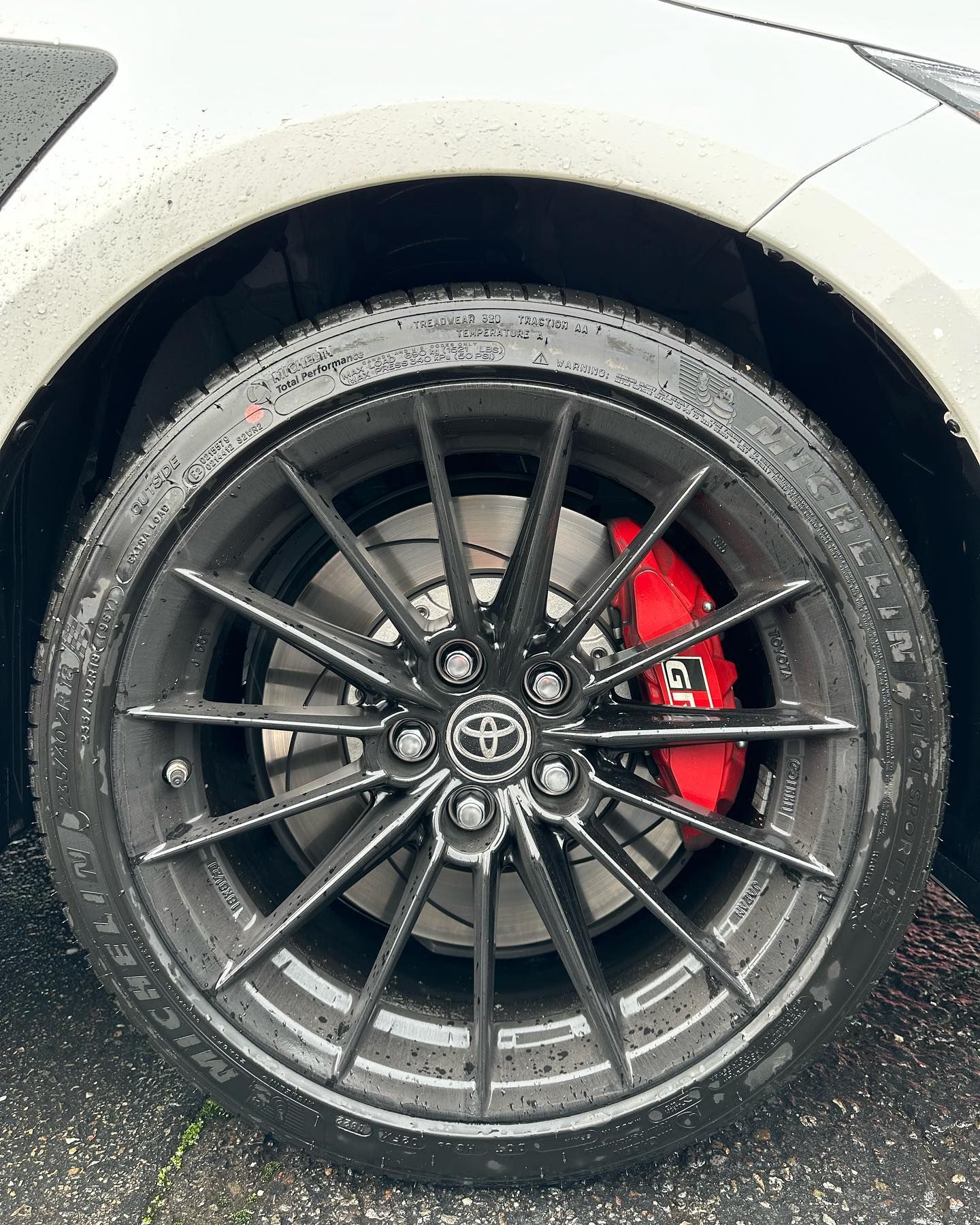 Close-up of a black Toyota wheel with red brake caliper on a wet road.
