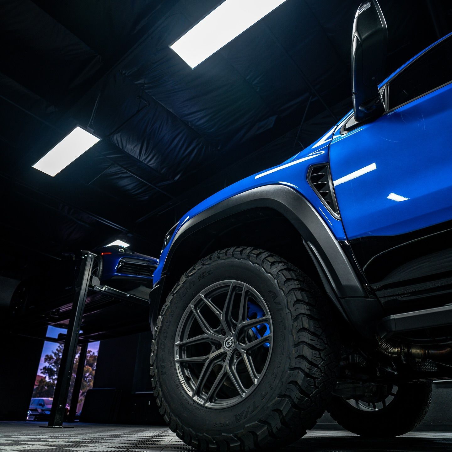 Blue off-road truck with large tires in a dark showroom, lit by overhead lights