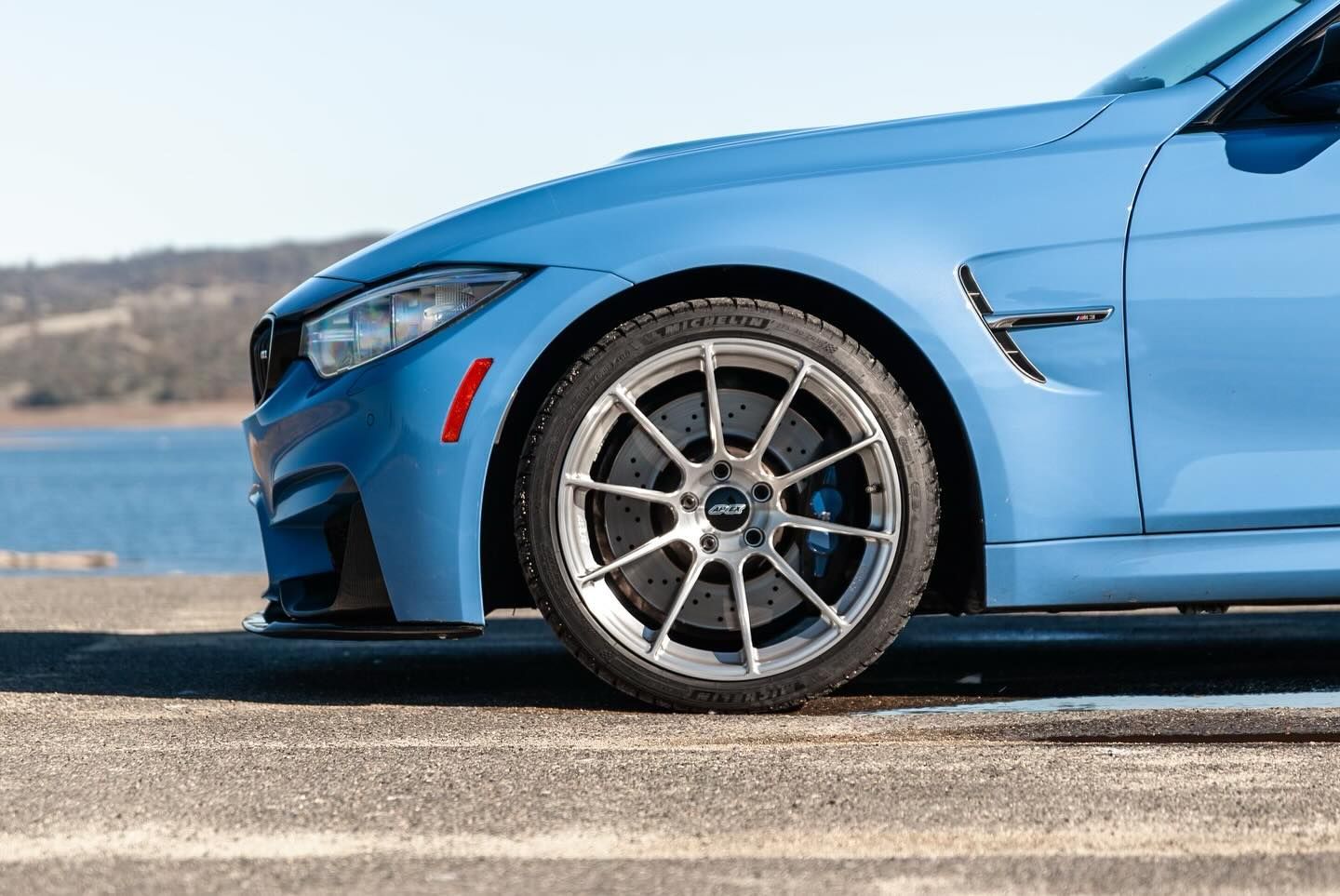 Blue sports car parked by the water, close-up of the front wheel and side panel.