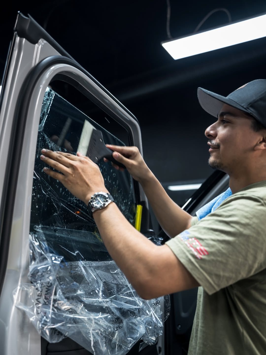 Man installing clear plastic film on a car door window inside a workshop