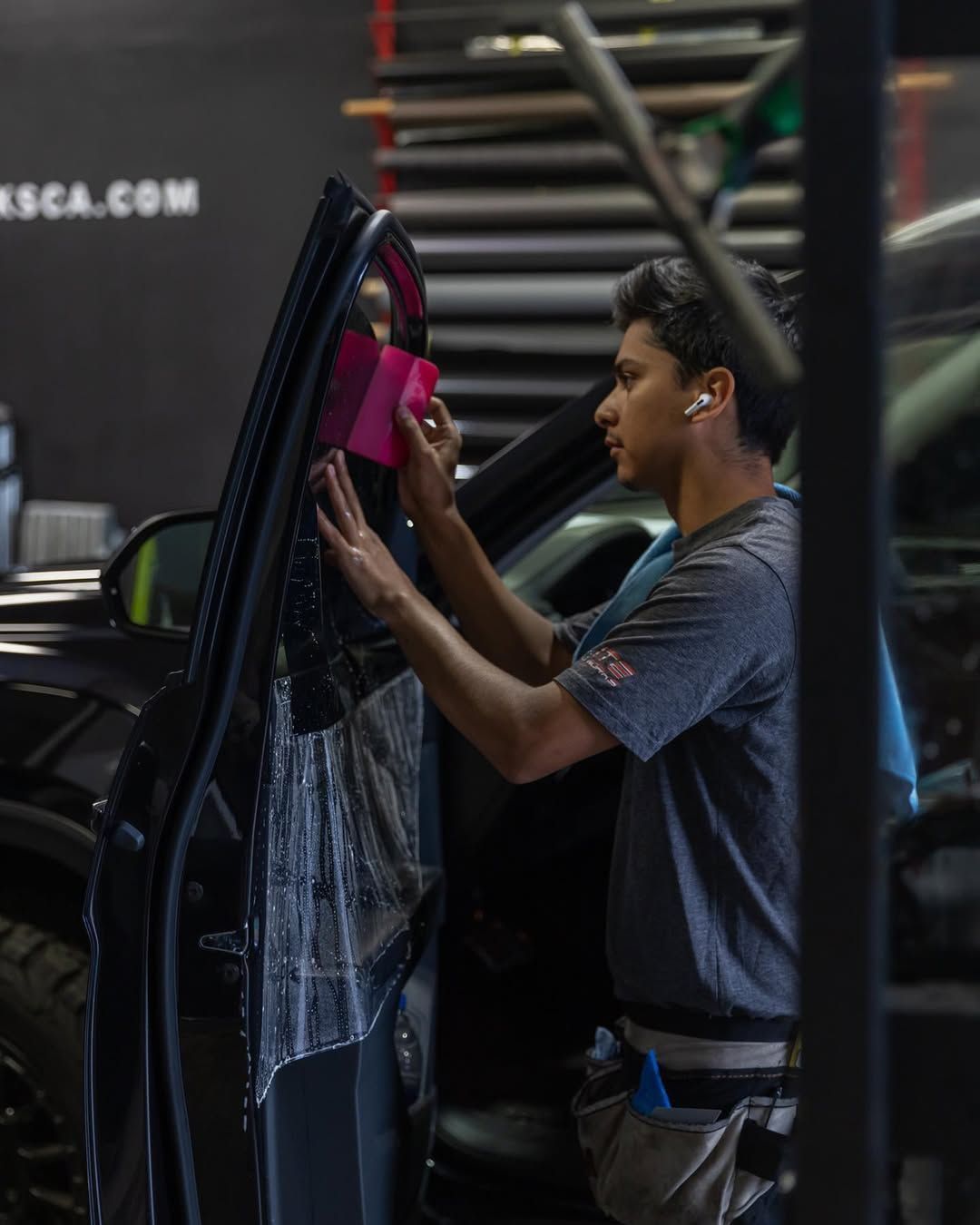 Person using a squeegee to clean a car window beside a ladder in a dim garage