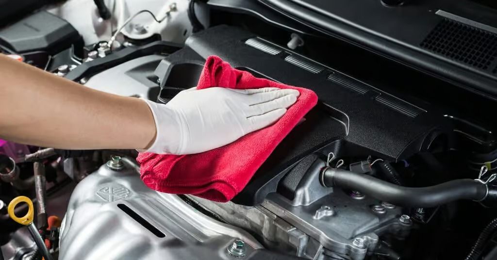 Gloved hand wiping a car engine with a red cloth under the hood