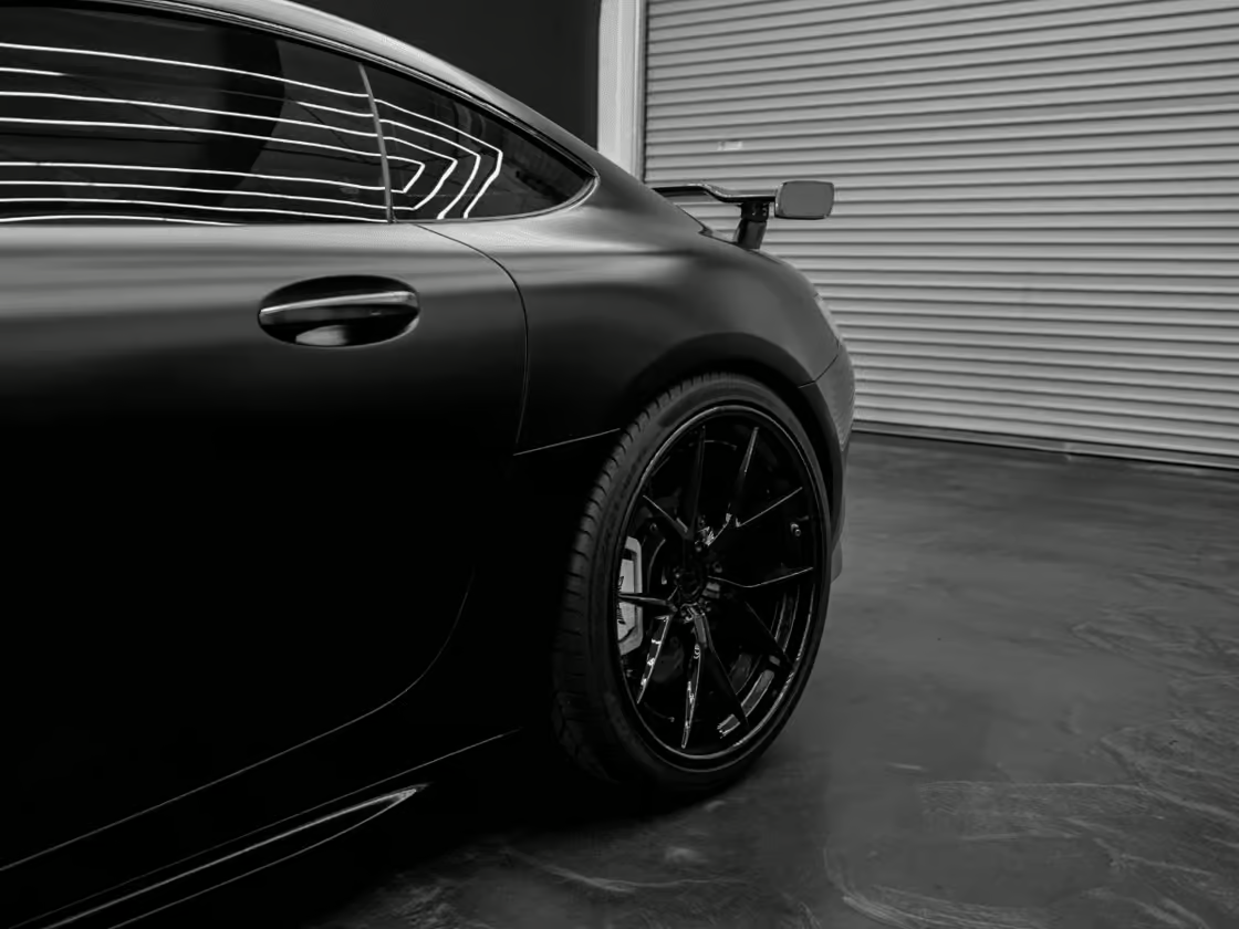 Black sports car rear side view with glossy finish and black rims in a garage.