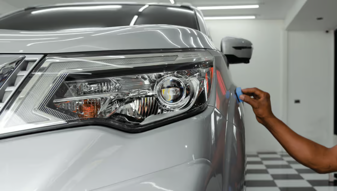 Car being detailed in a garage, with a hand cleaning the front headlight and hood.
