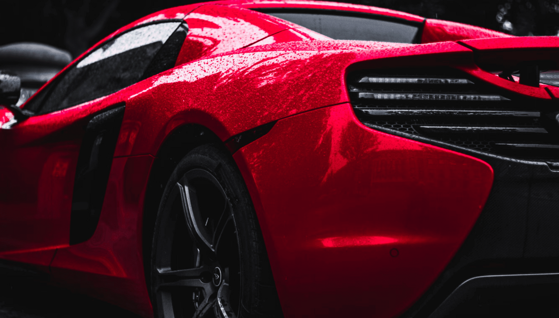 Rear view of a glossy red sports car with black accents in a dark studio setting