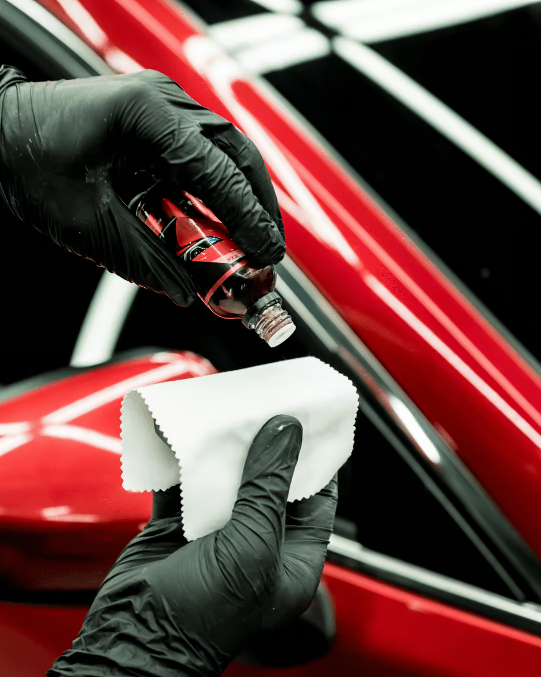 Gloved hands applying polish to a red car with a white cloth