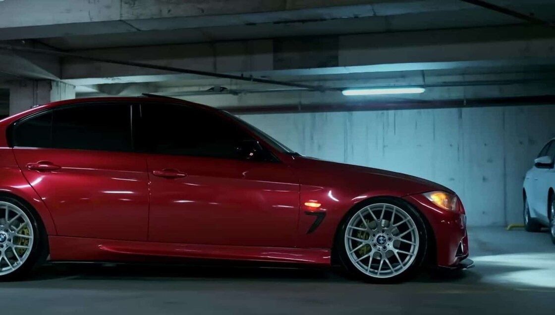 Red sports sedan parked in a dim underground garage, side view.