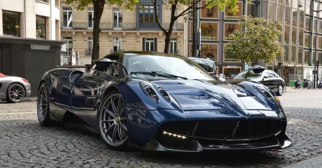 Dark blue sports car parked on a cobblestone street in front of buildings