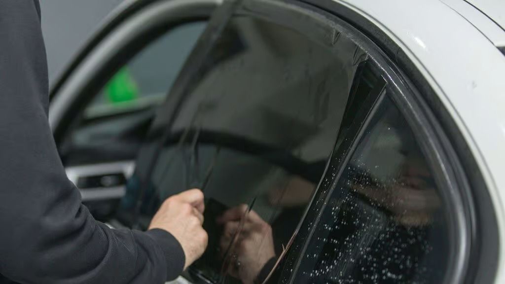 Person unlocking a white car door with a key, seen close up through the window