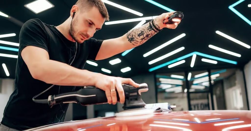 Mechanic polishing a red car in a garage, with bright overhead lights
