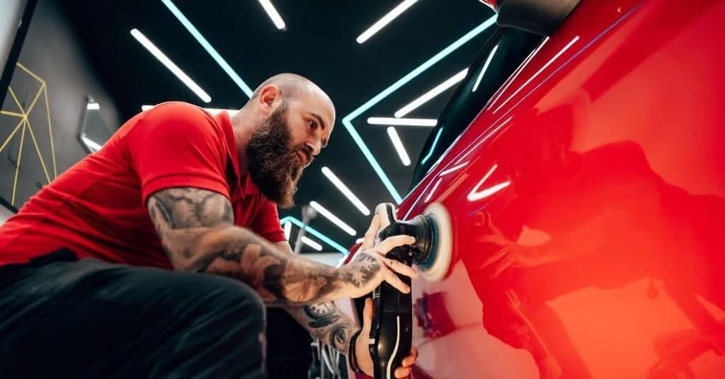 Tattooed mechanic polishing a red car in a neon-lit garage