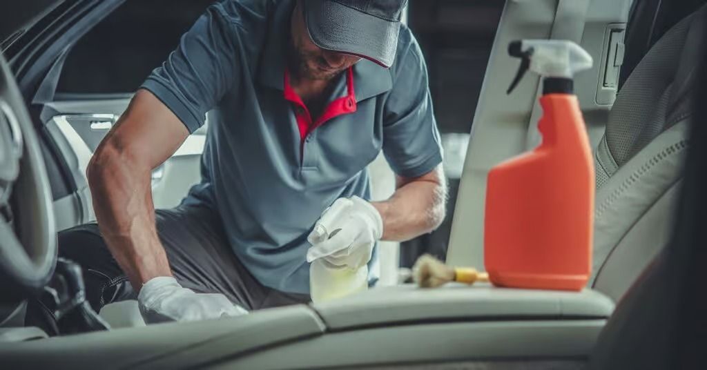 Person cleaning a car interior with spray bottle and cloth, with orange cleaner in foreground
