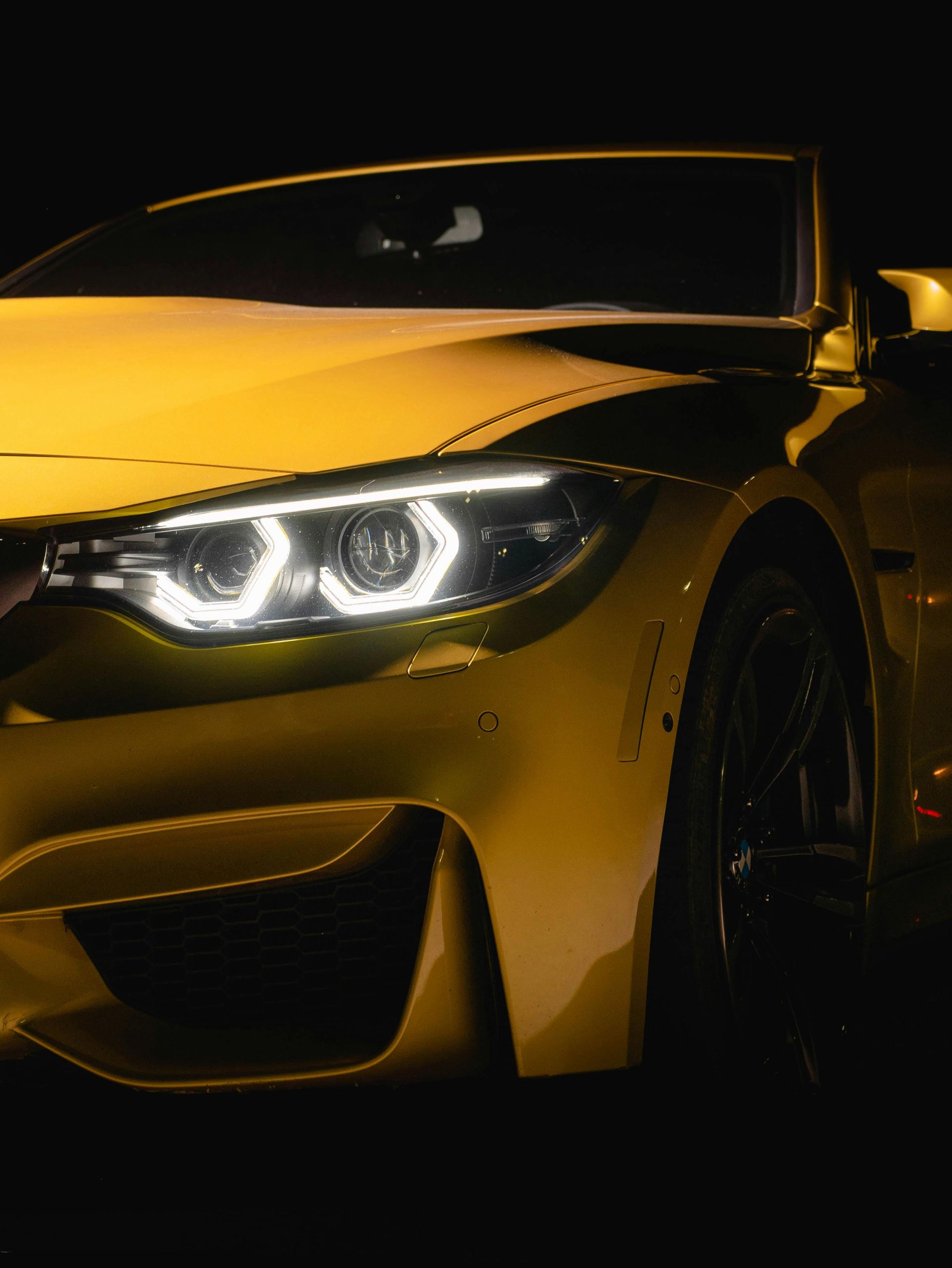 Yellow sports car front end with headlights on in a dark setting
