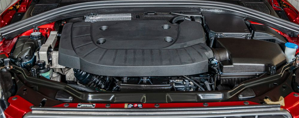 Car engine bay with a large black engine cover and red body panels along the sides and front.