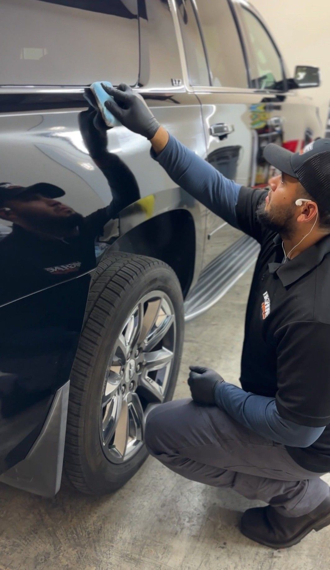 Technician cleaning a black SUV’s side panel with a cloth outdoors