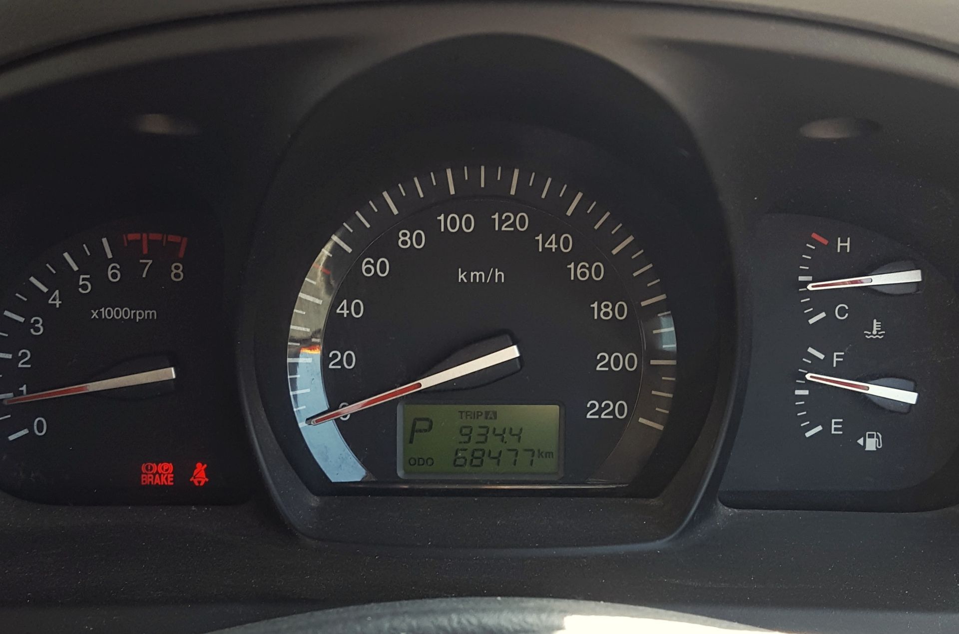 Car dashboard with speedometer and gauges, red warning lights on, green digital display visible.