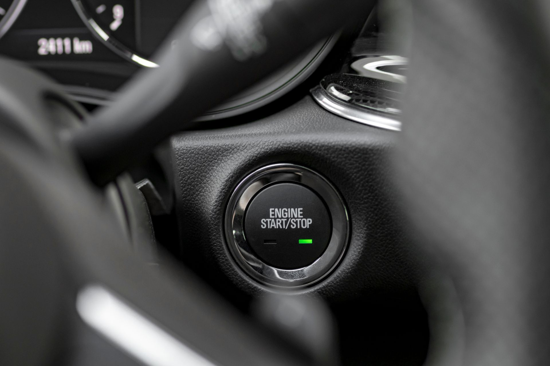 Close-up of a car's push-button ignition on a black dashboard, with a green indicator light.